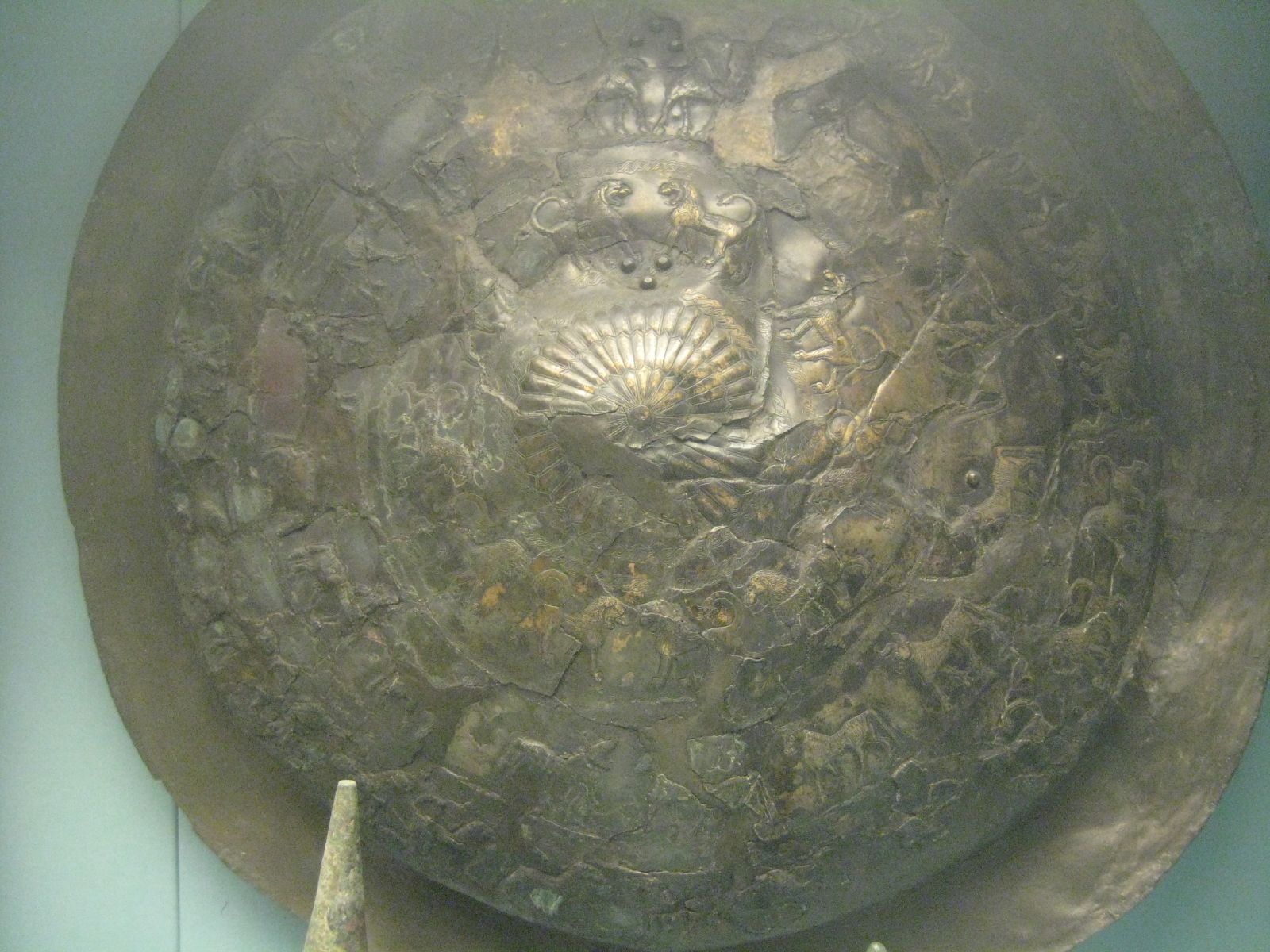 A round bronze shield, darkened with age, decorated with rows of incised lions and bulls around a raised central boss
